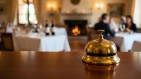 Elegant brass service bell on wooden counter in upscale restaurant dining room with fireplace and blurred guests enjoying fine dining experience.
