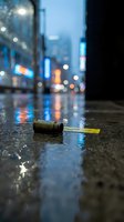 Empty glass bottle lying on wet city street at night with blurred urban lights and reflections creating atmospheric mood for environmental awareness campaigns.