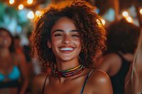 Young African American woman with curly hair smiling joyfully at night party with bokeh lights background for lifestyle and celebration content.