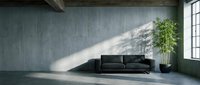 Modern black leather sofa in minimalist loft interior with concrete walls and natural light from large window, suitable for interior design and architecture projects.