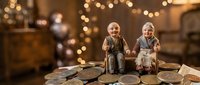 Elderly couple figurines sitting together on wooden surface with warm bokeh lights creating cozy atmosphere for home decor and gift concepts.