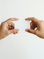 Two hands holding blank white card against neutral background, demonstrating product display, branding mockup, or business presentation concept.