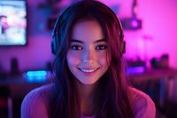 Young Asian woman wearing headphones smiling at camera in neon purple lighting, gaming setup with LED lights in background creates modern cyberpunk atmosphere.