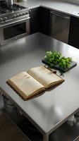 Open vintage cookbook with aged pages and fresh green herbs in planter on modern stainless steel kitchen counter with appliances, culinary inspiration and home cooking concept.