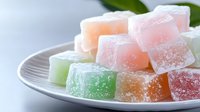 Colorful fruit jelly cubes with sugar coating arranged on white plate. Sweet gummy candy dessert in pastel colors for confectionery and treat concepts.