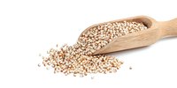 Raw quinoa grains in wooden scoop spilling onto white surface, showcasing nutritious ancient grain for healthy cooking and dietary recipes.