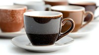 Ceramic coffee cups with dark espresso on white saucers arranged in row against light background, shallow depth of field creates artistic blur effect.