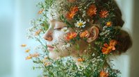 Young Caucasian woman with closed eyes in profile view, face adorned with delicate orange daisies and white baby's breath flowers creating dreamy spring portrait.