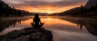 Woman meditating on rock by serene lake at golden sunset, surrounded by mountains and forest, peaceful mindfulness and nature retreat scene.