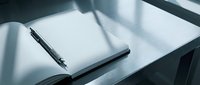 Open notebook with pen on white desk surface, minimalist workspace setup for business, writing, planning, and creative projects.
