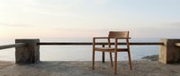 Wooden chair positioned on sandy beach at sunset with calm ocean and horizon in background, conveying solitude and contemplation for editorial and lifestyle design use.