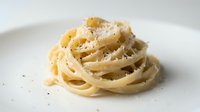 Nest of creamy pasta with grated cheese and black pepper on white plate, ready for restaurant menus, food blogs, cooking websites.
