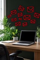 Red email icons floating above workspace with laptop and plants on wooden desk against dark green wall. Modern home office setup for digital communication.