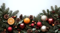 Fresh evergreen branches with red and silver ornaments, pine cones, orange citrus slices, and holly berries create festive Christmas border on white background.