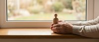 Elderly person holding wooden figurine on windowsill with natural light, symbolizing memories, nostalgia, and contemplation for editorial and lifestyle content.