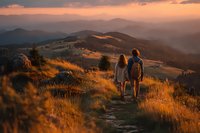 Two hikers walking on mountain trail at golden hour sunset with rolling hills and warm light creating peaceful outdoor adventure scene.