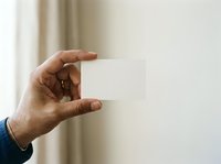 Hand holding blank white card against neutral background with soft natural light, suitable for business branding and marketing mockups.