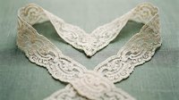 Delicate vintage lace collar with intricate floral patterns on soft green fabric background for fashion design and crafting projects.