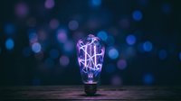 Neon glowing light bulb with purple and blue bokeh lights on dark background, representing innovation, technology, and creative ideas for design projects.