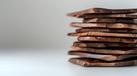 Broken dark chocolate pieces stacked in layers creating abstract geometric shapes against light background, macro food photography with selective focus.