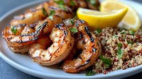 Grilled spicy shrimp served with quinoa grain side dish and fresh lemon wedges on gray plate, garnished with chopped herbs and seasonings.