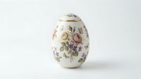 Elegant porcelain egg with delicate floral pattern featuring roses and botanical motifs on white background, decorative collectible ornament for Easter decor.