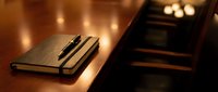 Closed notebook with pen on wooden desk surface with warm ambient lighting and blurred background for business and office concepts.