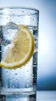 Glass of sparkling water with fresh lemon slice and ice cubes, condensation droplets on exterior, refreshing beverage for hydration, wellness, and lifestyle content.