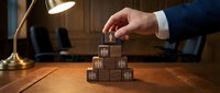 Businessman placing wooden block on pyramid structure at desk, representing business growth, strategy and risk management in corporate environment.