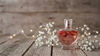 Heart-shaped perfume bottle with romantic floral arrangement on rustic wooden background with warm fairy lights for Valentine's Day celebration.
