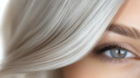 Close up view of platinum blonde hair and blue eye with natural makeup and long eyelashes against soft beige background, showing modern beauty and hair care concept.