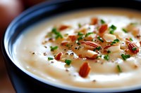 Creamy potato soup garnished with crispy bacon bits, fresh chopped chives and toasted pecans served in dark ceramic bowl, close up view with selective focus.