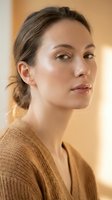 Young Caucasian woman with natural makeup and brown hair in casual sweater looking confident and serene in warm indoor lighting for lifestyle content.