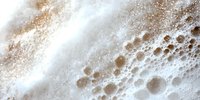Creamy coffee foam with bubbles and swirls in macro photography showing rich texture and natural patterns of fresh brewed cappuccino surface.