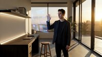 Young Asian man interacting with holographic interface in modern smart home kitchen at sunset with city view through floor-to-ceiling windows.