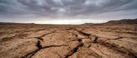 Cracked earth and parched ground under stormy skies depict severe drought conditions, climate change impacts, and environmental degradation for editorial and awareness campaigns.