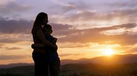 Silhouette of loving couple embracing at sunset with dramatic sky and mountain landscape. Romantic moment during golden hour for relationship concepts.