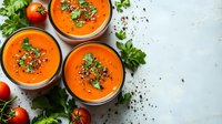 Fresh homemade tomato soup garnished with herbs and spices served in individual portions on light background, top view with copy space for menu or recipe.