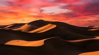 Desert sand dunes at sunset with dramatic orange and red sky, golden light casting shadows across rolling landscape for travel and nature backgrounds.