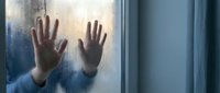 Young woman pressing hands against foggy glass window during rainy day, expressing loneliness and contemplation in moody atmospheric lighting.