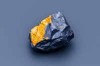 Raw black stone with golden metallic surface detail on gray background, isolated mineral specimen showing contrast between rough and shiny textures.
