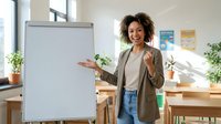 Smiling African American businesswoman presenting at whiteboard in modern office conference room for corporate training and professional development.