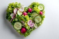 Fresh green salad arranged in heart shape with cucumber slices, radishes and mixed lettuce leaves on white background for healthy eating concept.