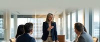 Confident senior Caucasian businesswoman leading team meeting in modern office, presenting strategy to diverse colleagues at conference table.