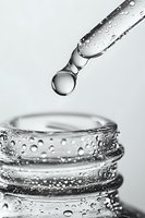 Water droplet falling from dropper into glass container with condensation and bubbles, captured in black and white macro photography. Medical research concept.