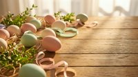 Pastel colored Easter eggs with ribbons and fresh greenery arranged on rustic wooden table in soft natural sunlight for spring holiday celebrations.