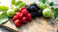 Fresh mixed berries and gooseberries on rustic wooden board with green leaves for healthy eating and organic food concepts.