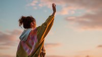 Young woman raising arms celebrating freedom success at sunset sky with pink clouds achieving goals personal growth motivation lifestyle wellness.