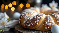 Fresh braided sweet bread sprinkled with powdered sugar on dark background with white flowers and bokeh lights, traditional Easter baking composition.