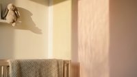 Minimalist nursery interior with soft natural light casting shadows on pale walls, featuring a wooden crib with knit blanket and teddy bear toy for newborn care design.